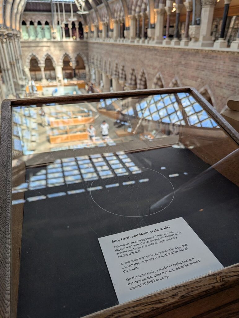Mond und Erde aus einem Maßstabsgetreuen Model von Sonne Mond und Erde. Die Sonne ist auf der gegenüberliegenden Seite des Naturkundemuseum als goldener Schimmer erkennbar.